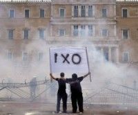 En medio de los gases lacrimógenos lanzados por la policía, dos manifestantes sostienen una pancarta que dice 'no' frente a la sede del Parlamento griego. Foto AFP