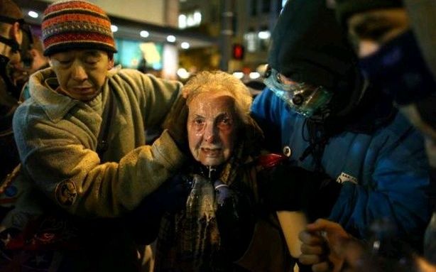 Dorli Rainey, una mujer de 84 años es acompañada por dos Ocupa con la cara cubierta totalmente de aerosol de gas pimienta.