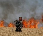 Soldado israelí porta una manguera mientras camina a través de un campo incendiado cerca de la frontera entre Israel y Gaza, el 14 de mayo de 2018.