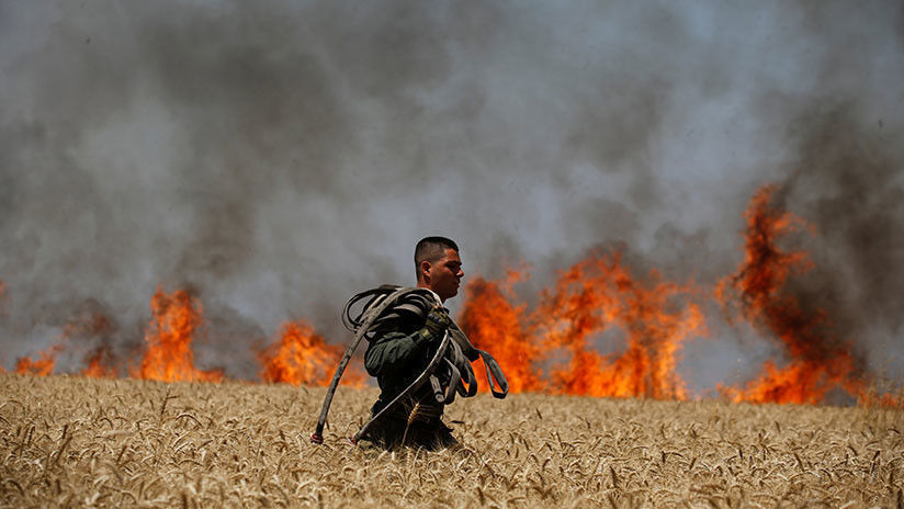 Soldado israelí porta una manguera mientras camina a través de un campo incendiado cerca de la frontera entre Israel y Gaza, el 14 de mayo de 2018.